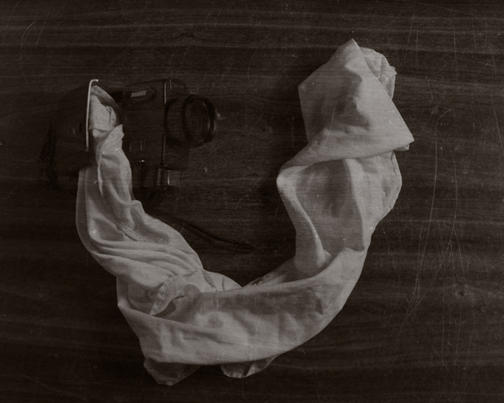 A semi-transparent super 8 camera and piece of cloth on a wooden surface